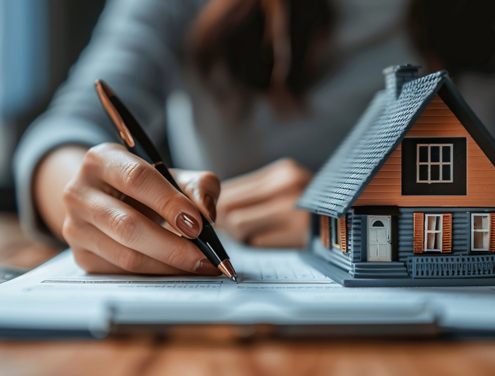 Hand writing on a document, a house on the desk next to them